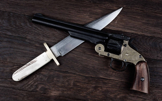 A holiday gift idea for collectors: a vintage replica revolver with a brass frame and wooden grip, crossed with a classic Bowie knife on a dark wood table.