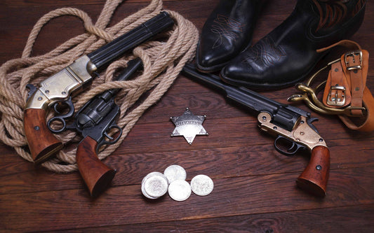 A flat lay of creative, Western-themed gift ideas showing replica revolvers, a sheriff's badge, cowboy boots, and a lasso on a dark wood table.