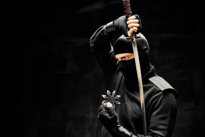 Ninja in black holding a katana, point down with a solid black background. 